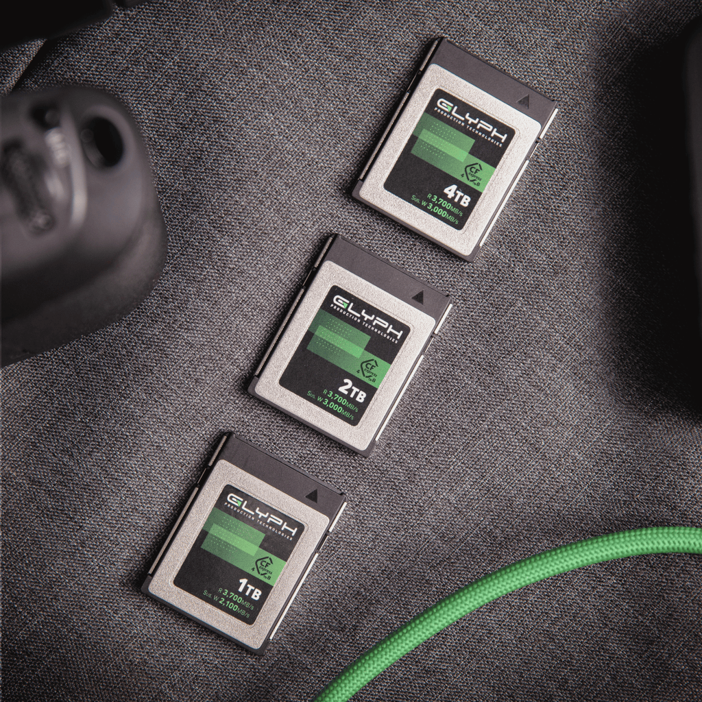 Three Glyph memory cards of different capacities on a textured surface with a green cable.