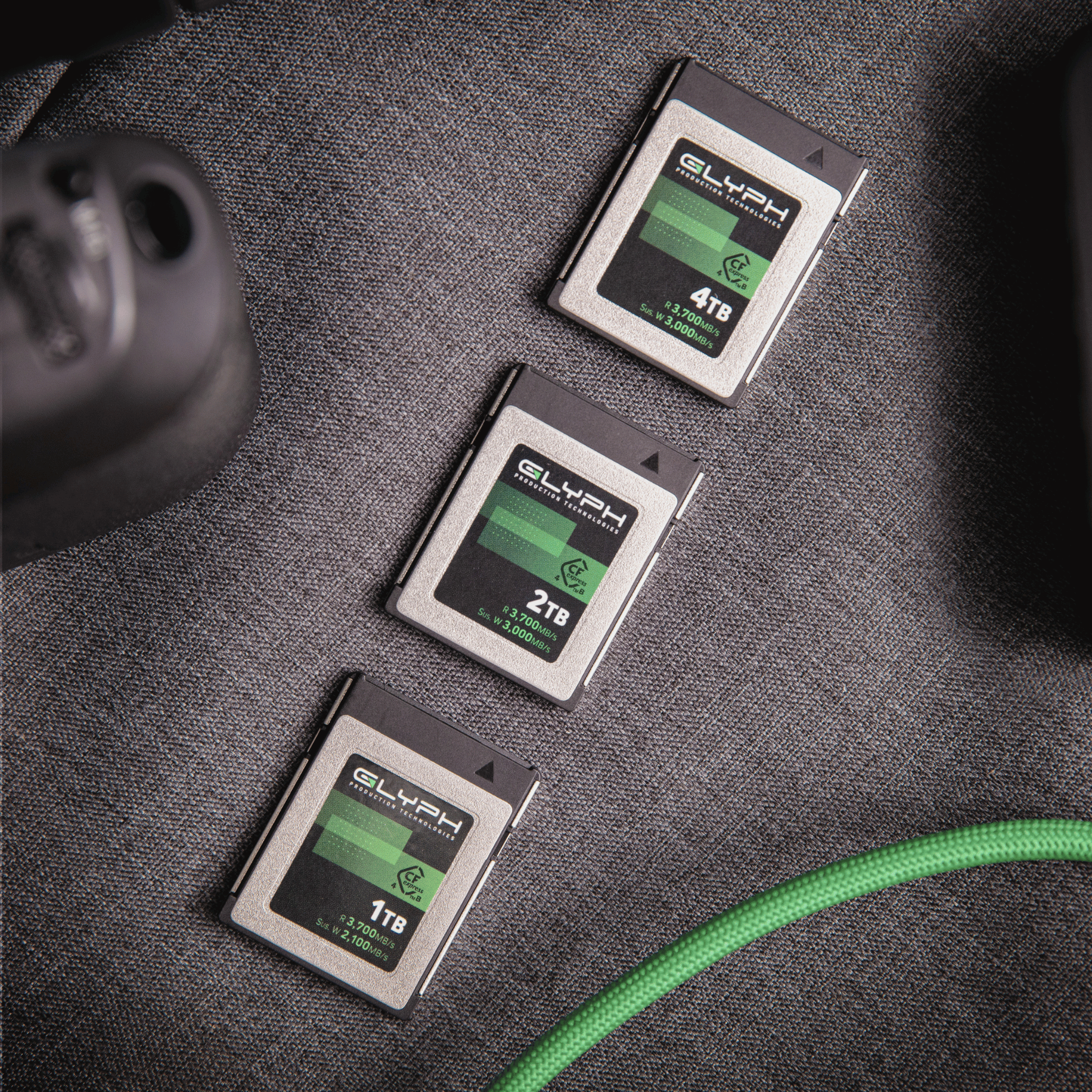 Three Glyph memory cards of different capacities on a textured surface with a green cable.