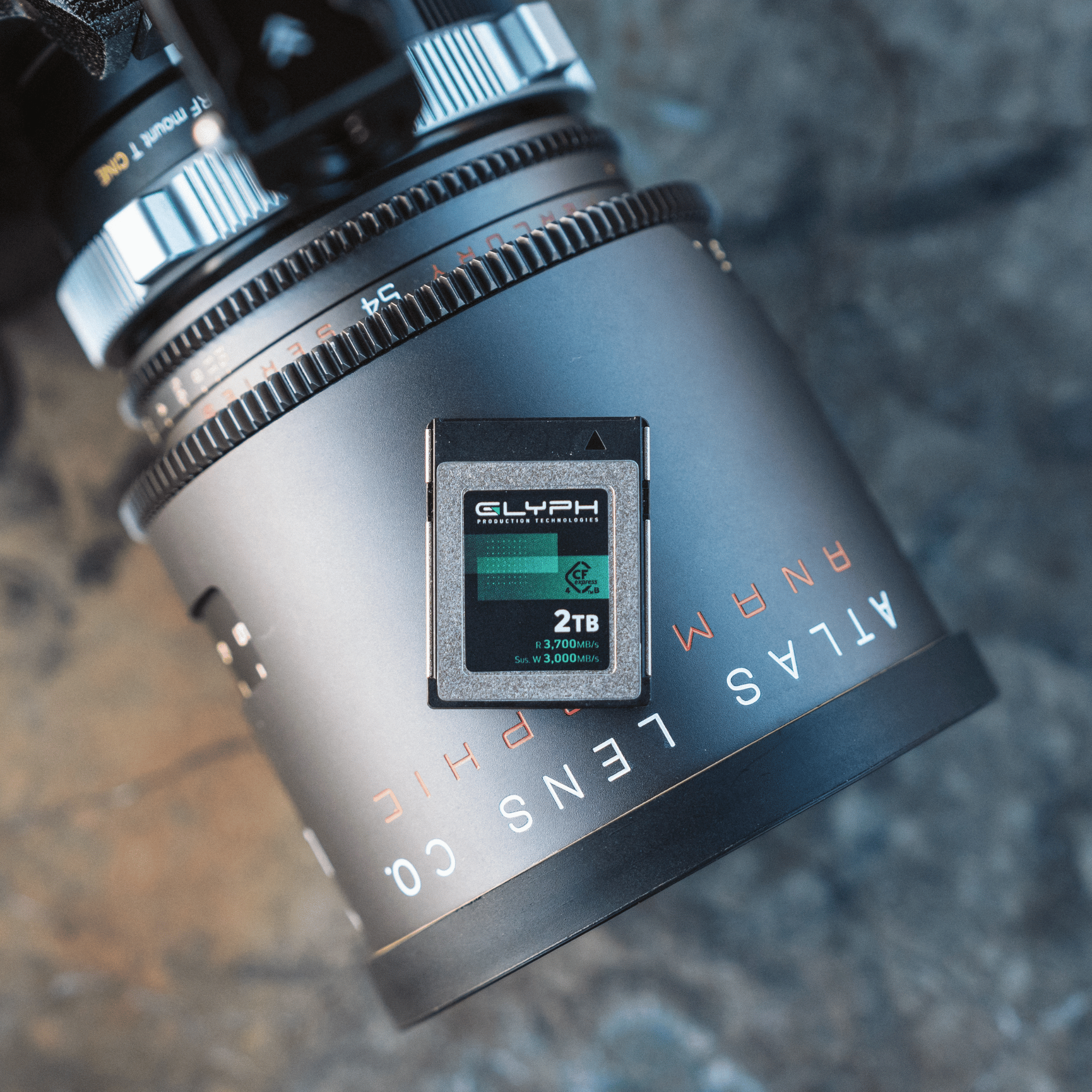 Camera lens with a Glyph 2TB CFexpress memory card on a textured surface