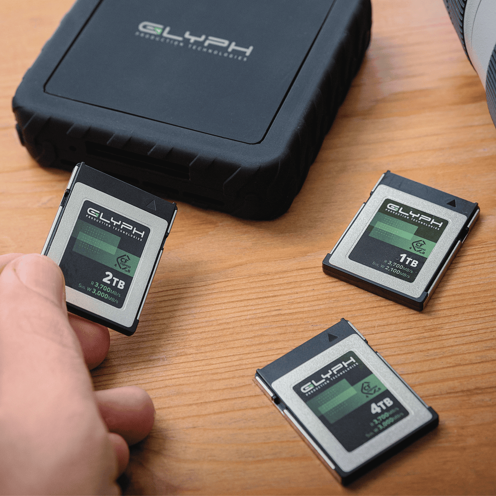 Three Glyph memory cards on a wooden surface with a hand holding one of them.